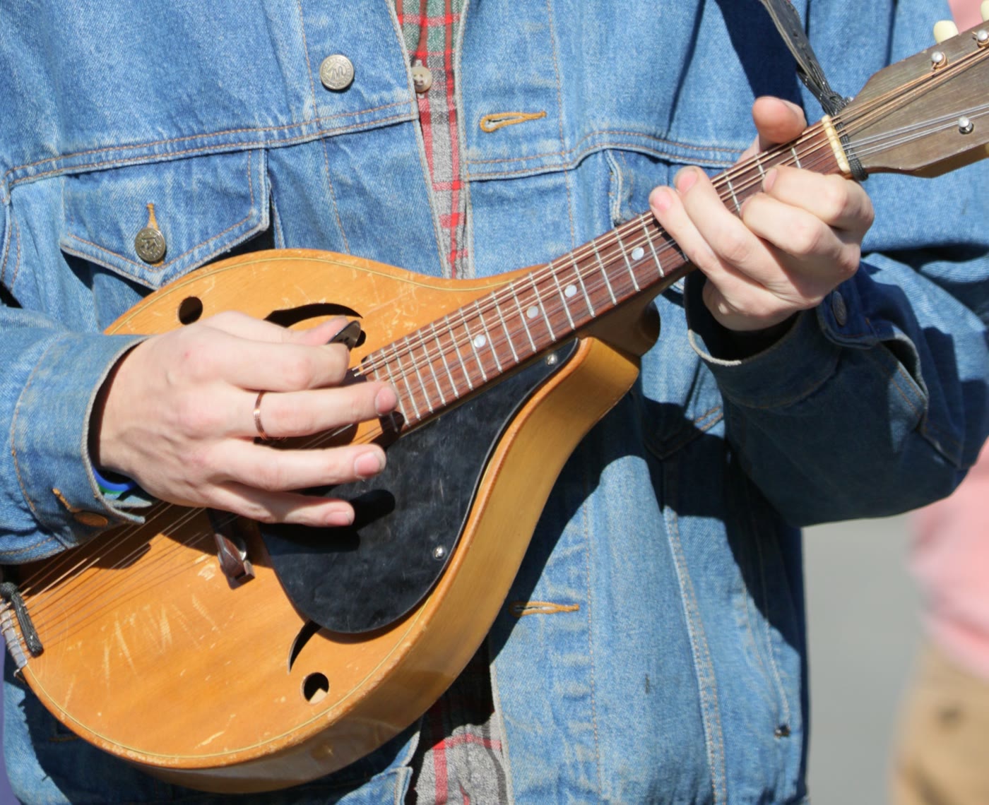 A relaxed right hand strumming an A-style mandolin with a pick, fretting hand on the neck